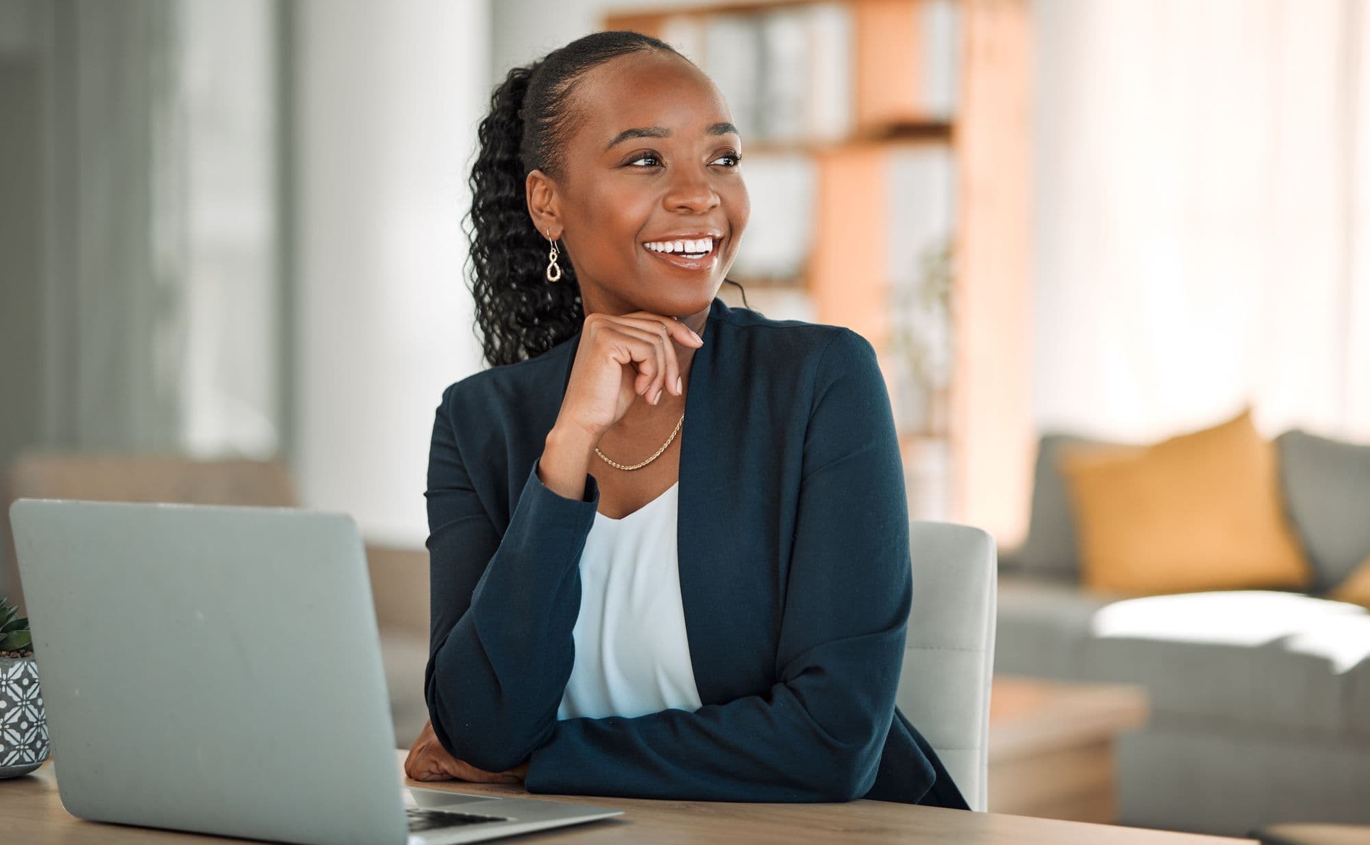 A woman in a blazer works at a laptop in a bright room